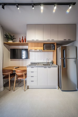 Eine kompakte Küche mit integriertem Mikrowellenherd, einem Edelstahlkühlschrank und einer kleinen Essecke mit Tisch und Stühlen.