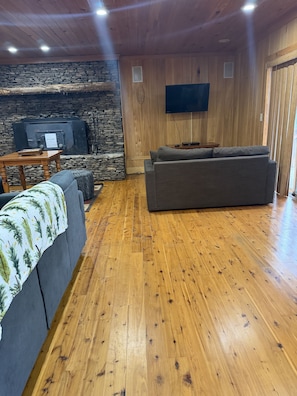 Ein Wohnzimmer mit Kamin aus Stein, Holzwänden, einem Flachbildfernseher, einem grauen Sofa und Holzboden.