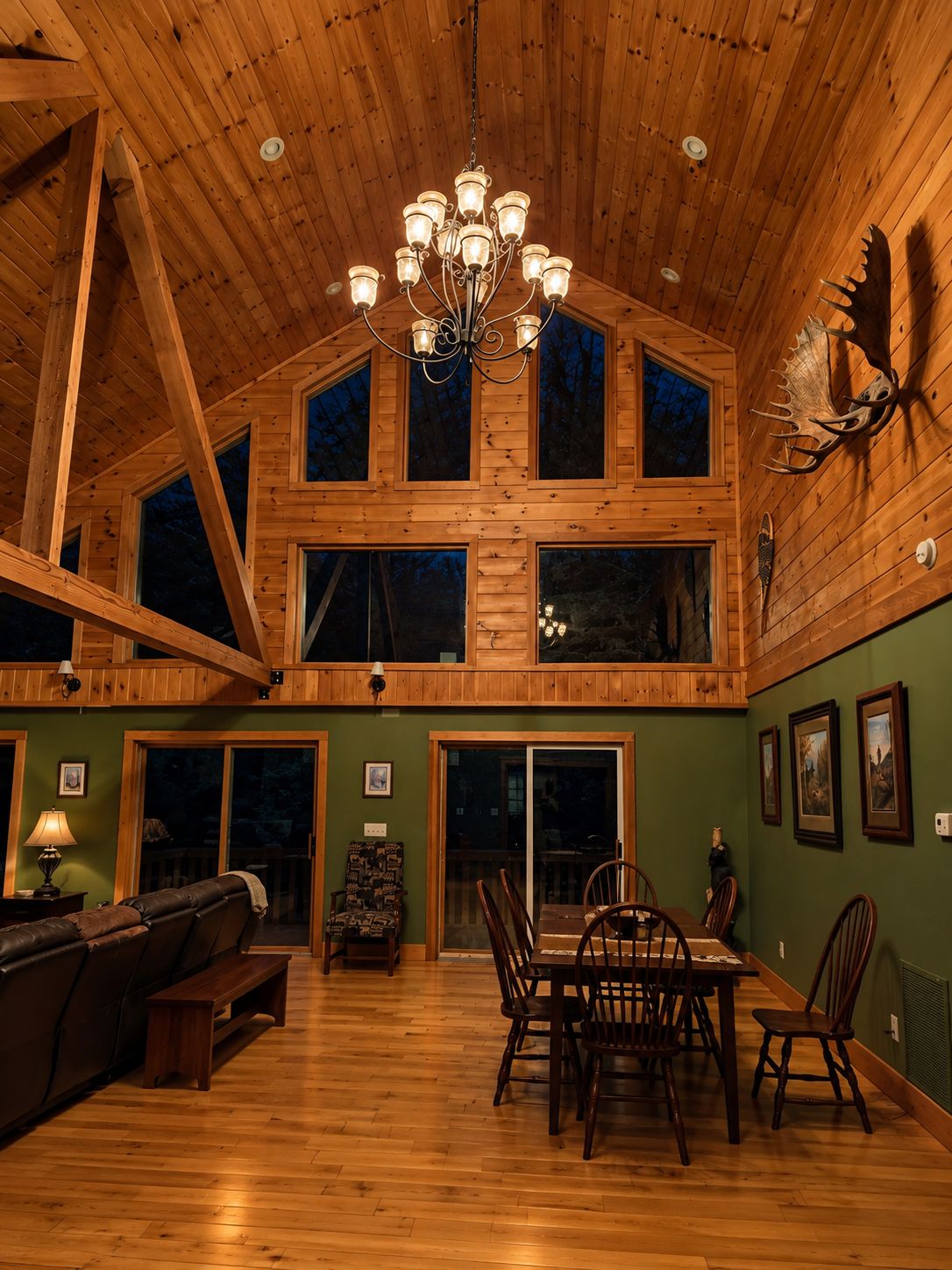 A spacious interior with a high ceiling, a dining area with wooden chairs, a sofa, and a chandelier.