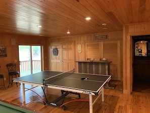 Ein Tischtennistisch in einem Holzraum mit einer Tür, einem Dartboard und einem Schild mit der Aufschrift 'BEER'.