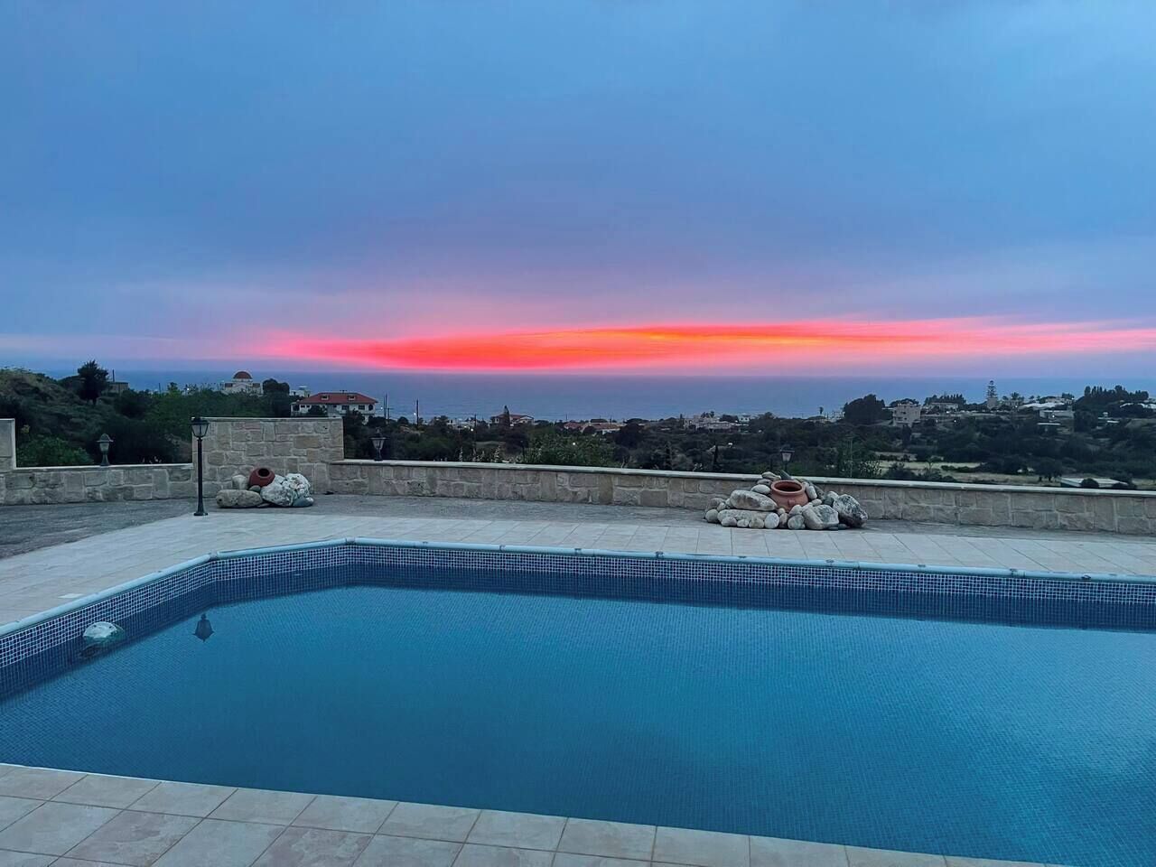 Ein Schwimmbad mit Blick auf einen Sonnenuntergang über einer Küstenstadt.