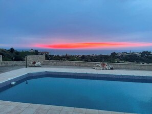 Ein Schwimmbad mit Blick auf einen Sonnenuntergang über einer Küstenstadt.