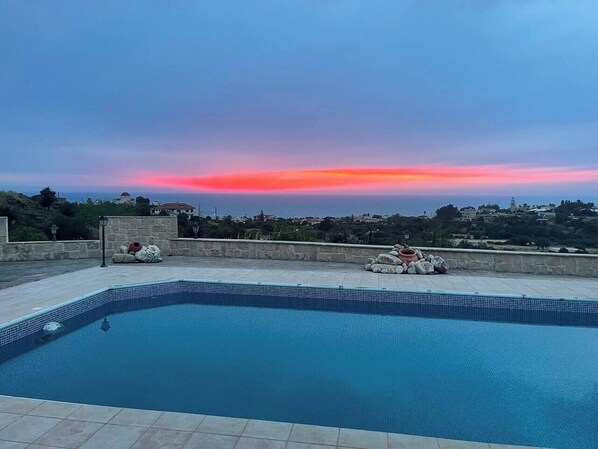A swimming pool with a view of a sunset over a coastal town.