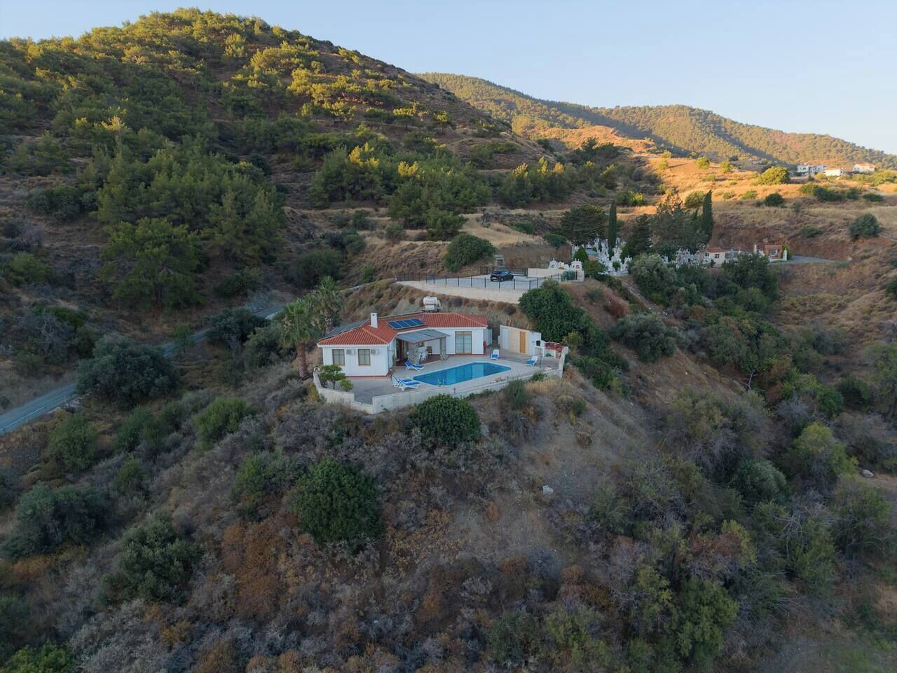 A single-story house with a swimming pool, surrounded by hills and sparse vegetation.