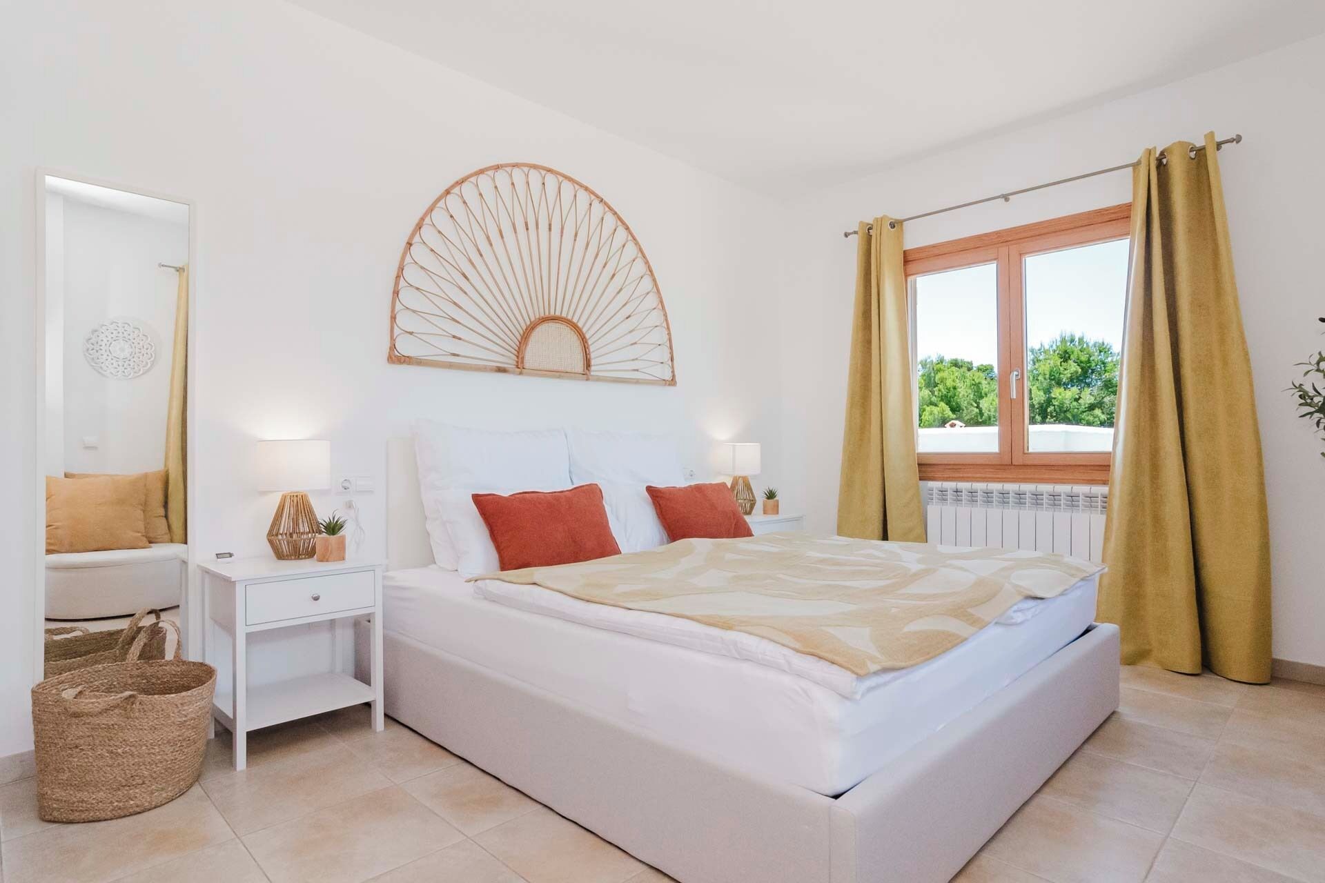 A bedroom with a bed, nightstands, a mirror, a window with curtains, and a wall decoration.
