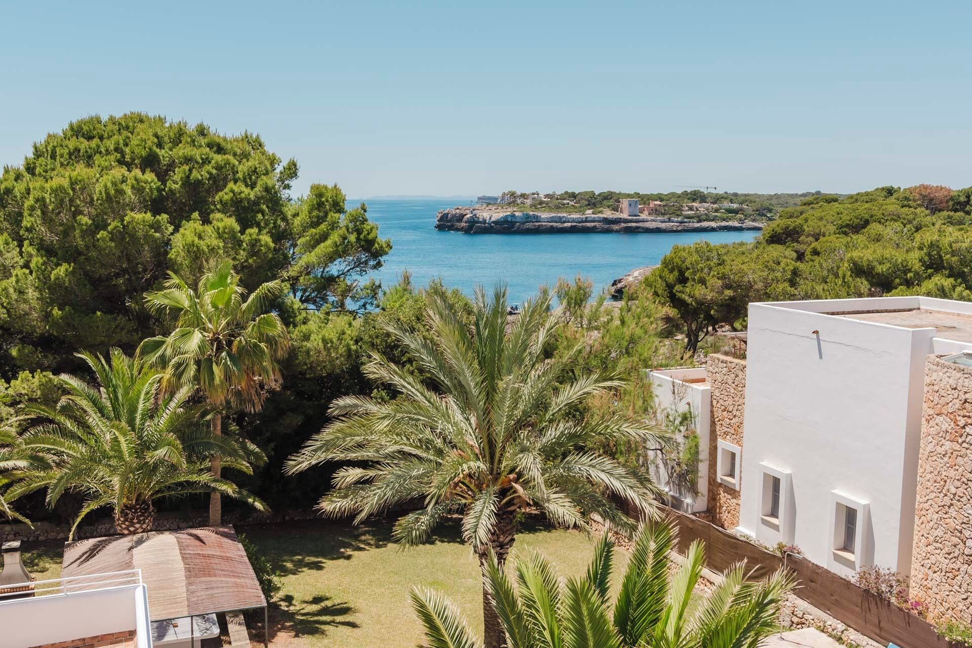 A coastal property with a view of the sea, palm trees, and a white building with windows.