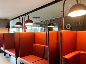 A row of orange cushioned seating with overhead lighting. - Acqua by Hosppedar (João Pessoa)