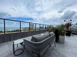 A rooftop terrace with a sofa, a small table, and potted plants. - Acqua by Hosppedar (João Pessoa)