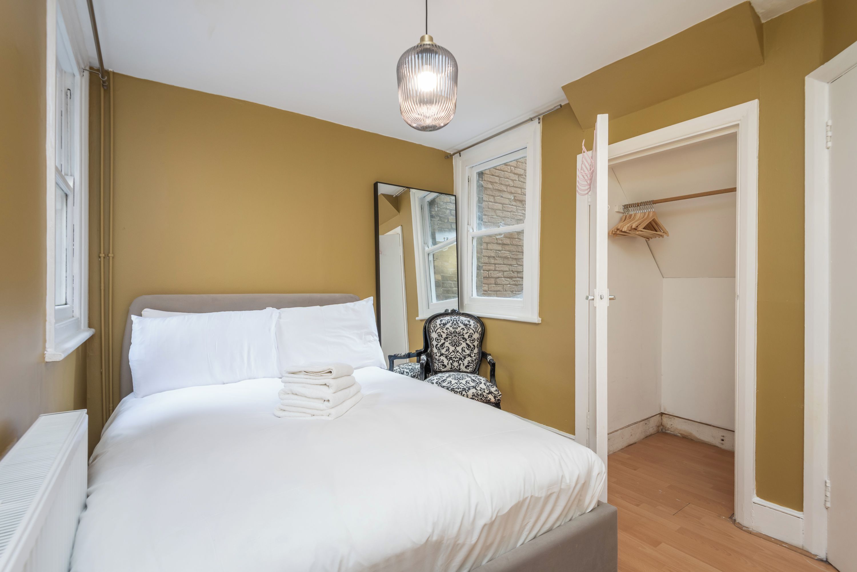 Un dormitorio con cama, una silla, un armario y una lámpara colgante.