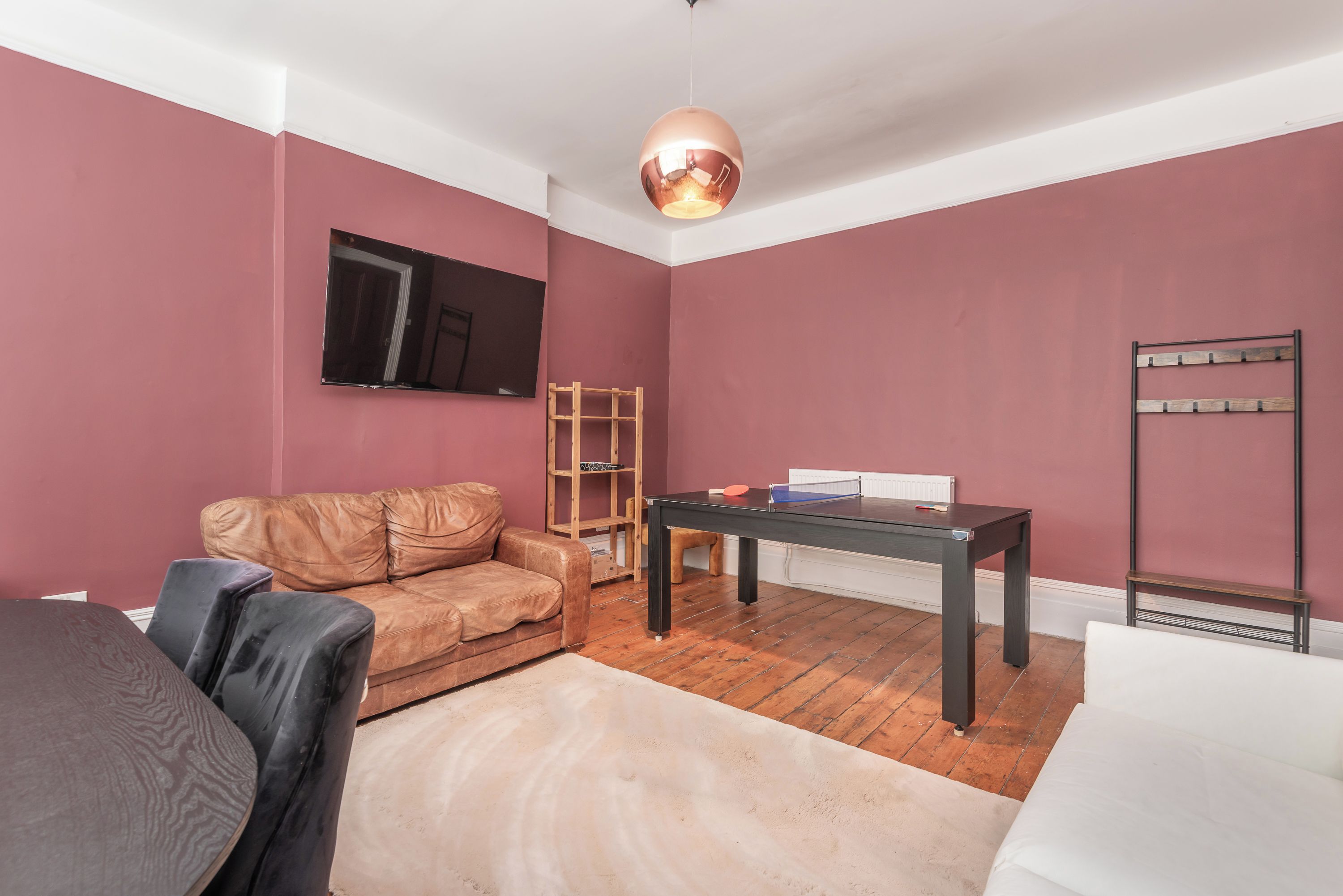Une pièce avec un canapé en cuir marron, une table servant également de table de ping-pong, une étagère en bois et un radiateur blanc.