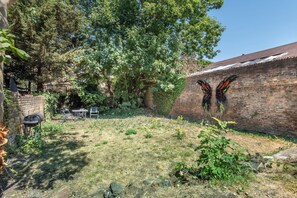 Ein Garten mit Ziegelmauer, Grill und einem großen Baum.