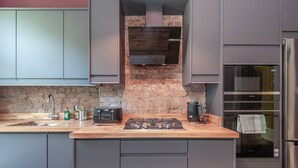 Cozinha moderna com armários cinza, painel de backsplash de tijolo, coifa Bosch, forno Siemens e bancada de madeira.