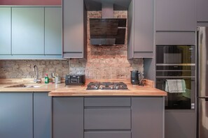 Eine moderne Küche mit grauen Schränken, einer Ziegelrückwand, einer Bosch-Dunstabzugshaube, einem Siemens-Backofen und einer Holzarbeitsplatte.