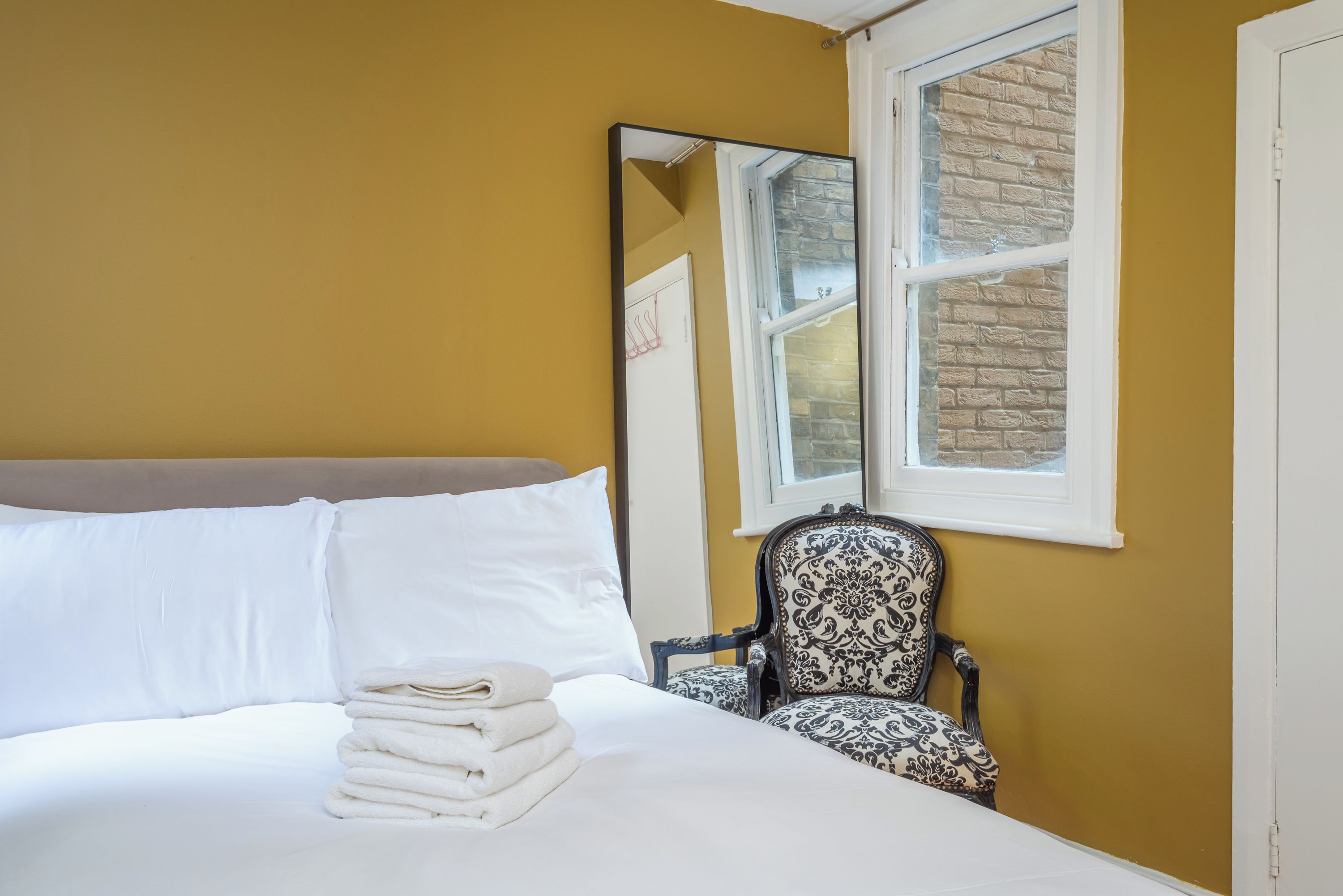 A hotel room with a bed, a chair, a window, and a mirror.