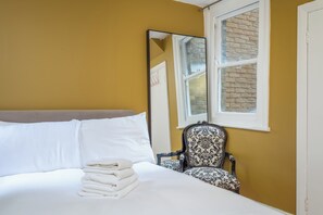 Una habitación de hotel con cama, silla, ventana y espejo.