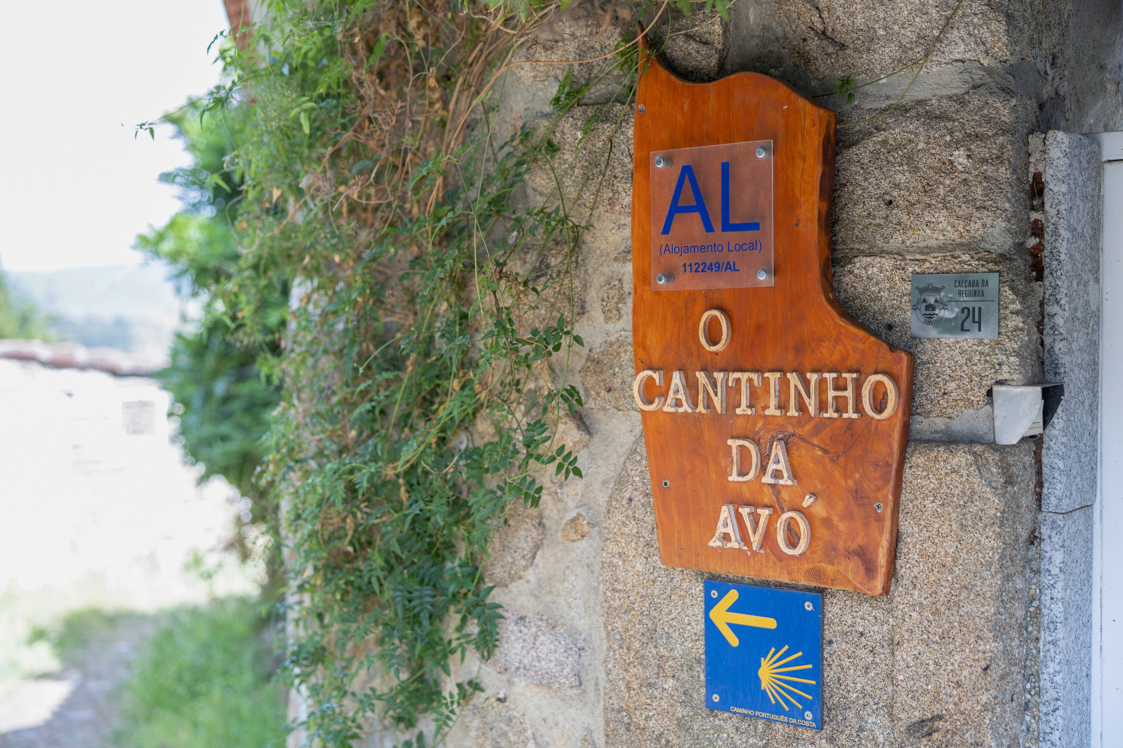 Un letrero de madera con el texto 'AL O CANTINHO DA AVO' y una señal azul direccional con una flecha.