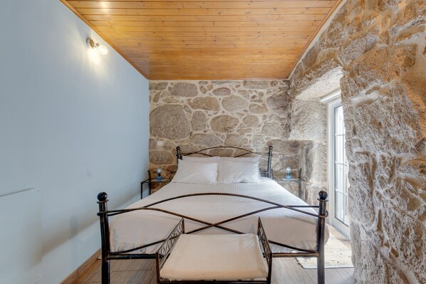 A bedroom with a stone wall, a wooden ceiling, and a metal bed frame.