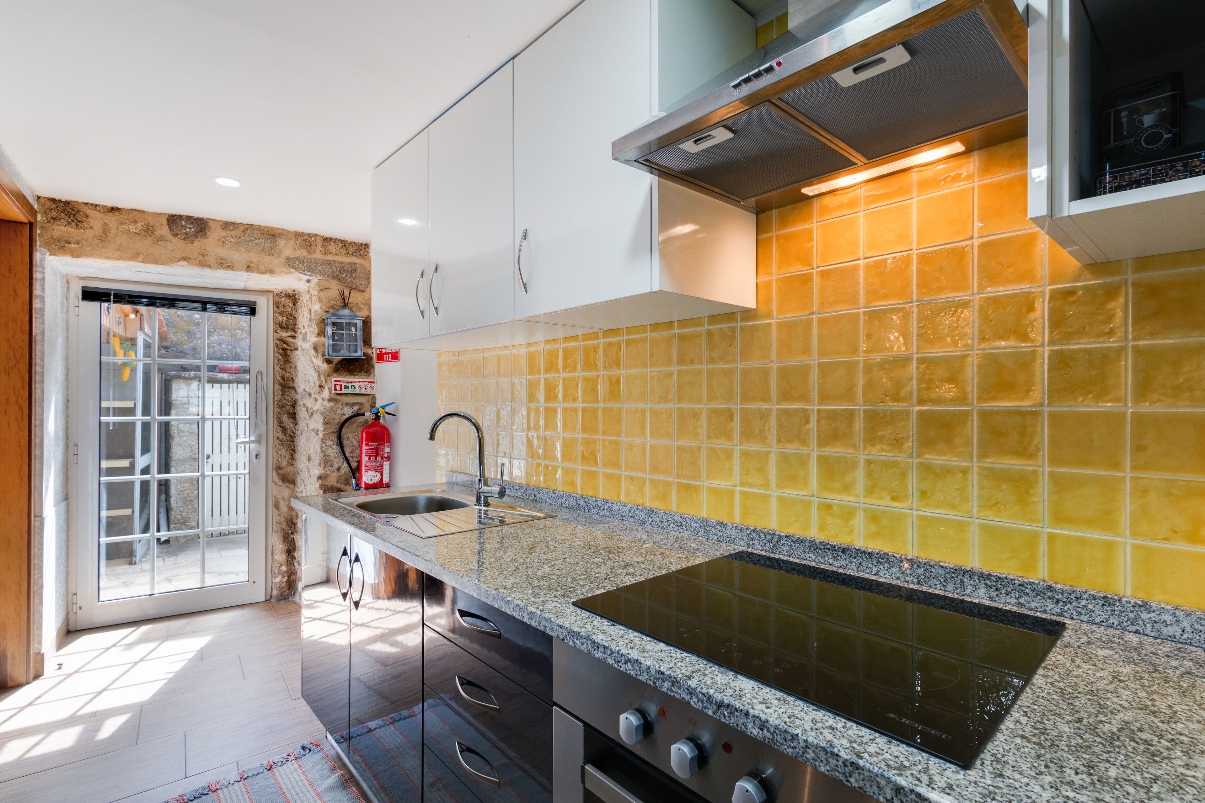 Una cocina moderna con estufa integrada, armarios de acero inoxidable y un salpicadero de azulejos amarillos.