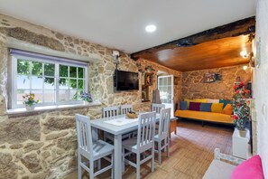 Una habitación con paredes de piedra, una mesa de comedor con sillas, un sofá y un televisor montado en la pared.