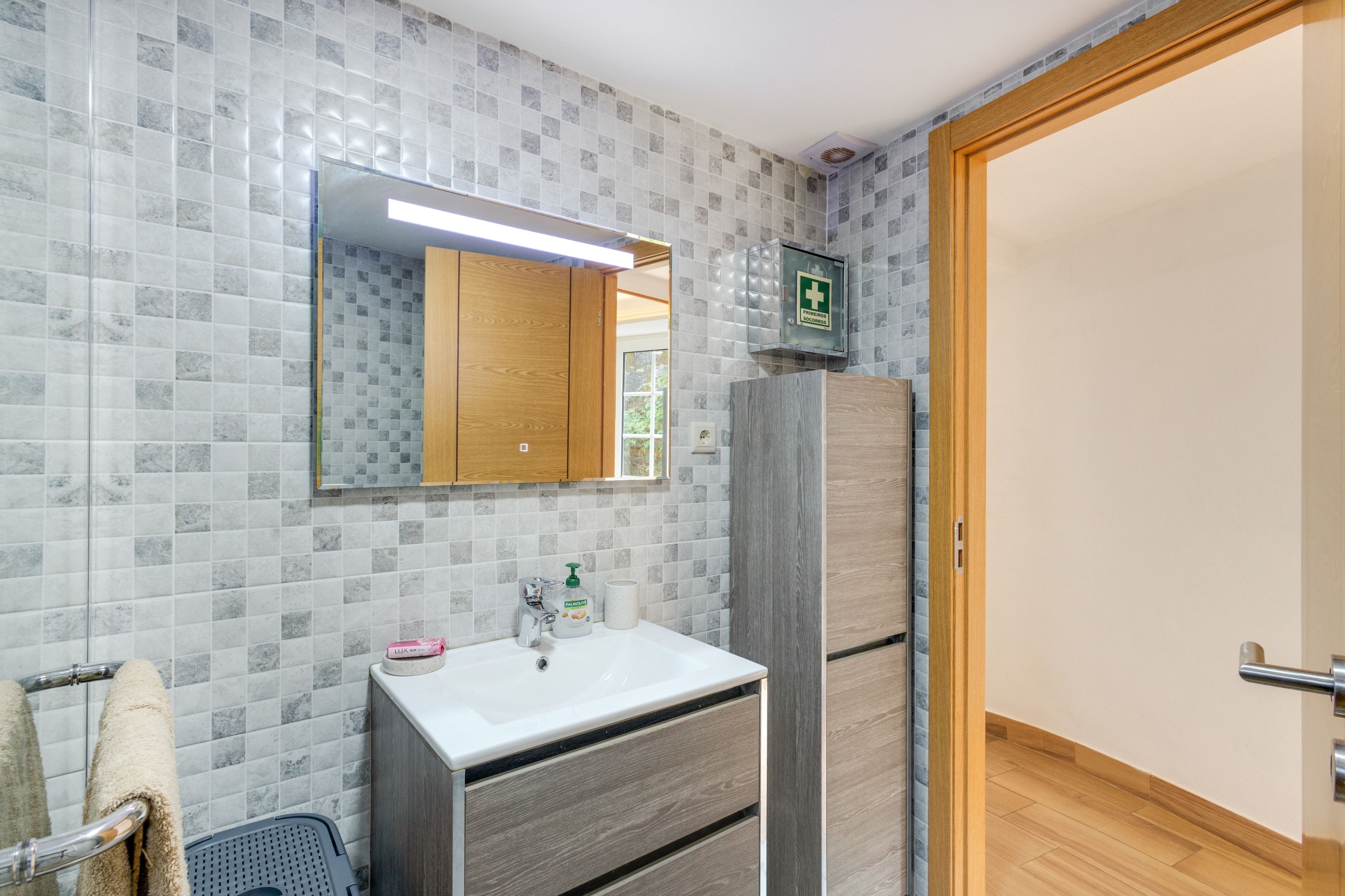 Een badkamer met een witte wastafel, een spiegel en een kastje.