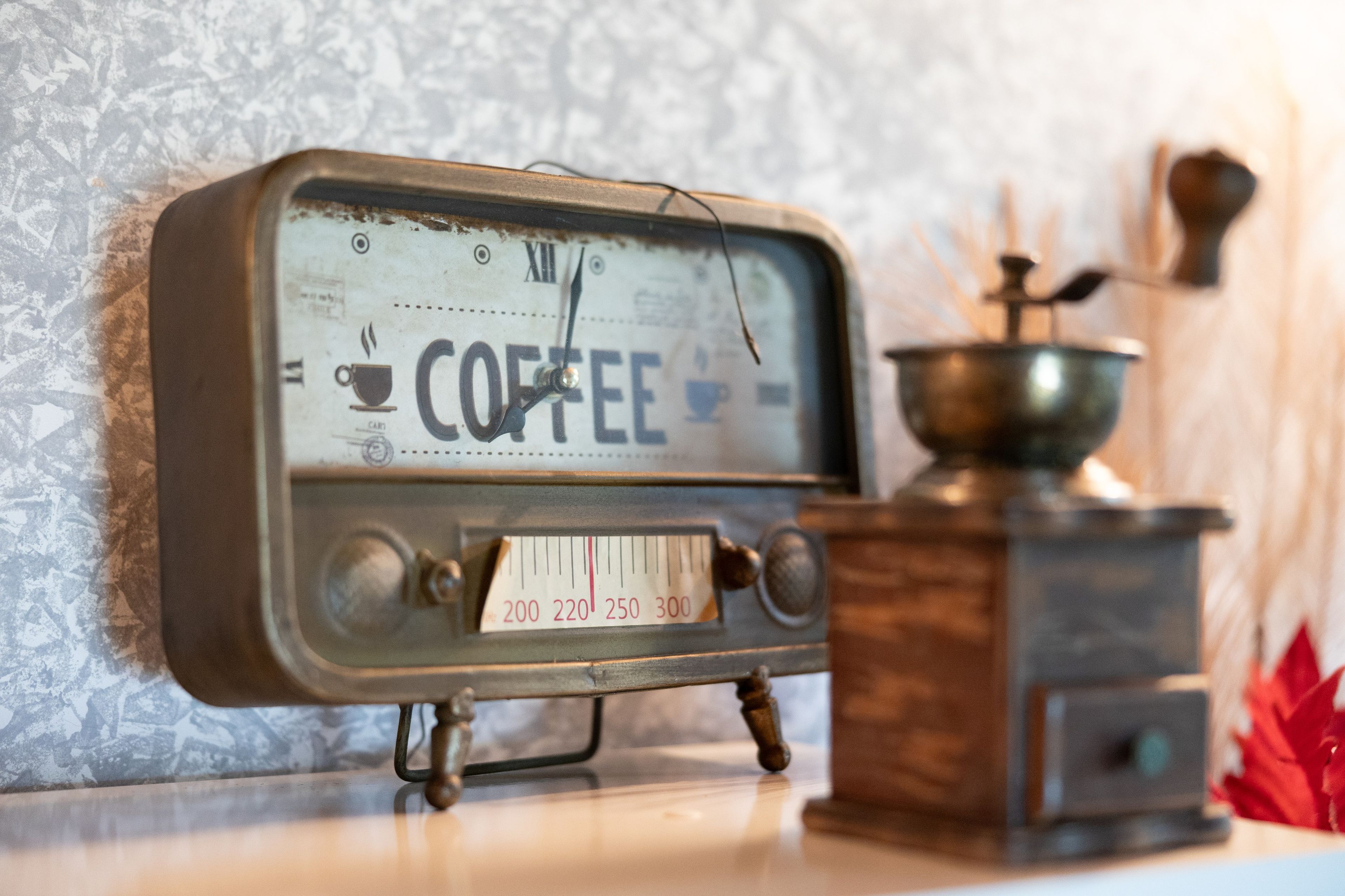 Une vieille machine à café dotée d’une horloge, placée devant un mur recouvert d’un papier peint à motifs.