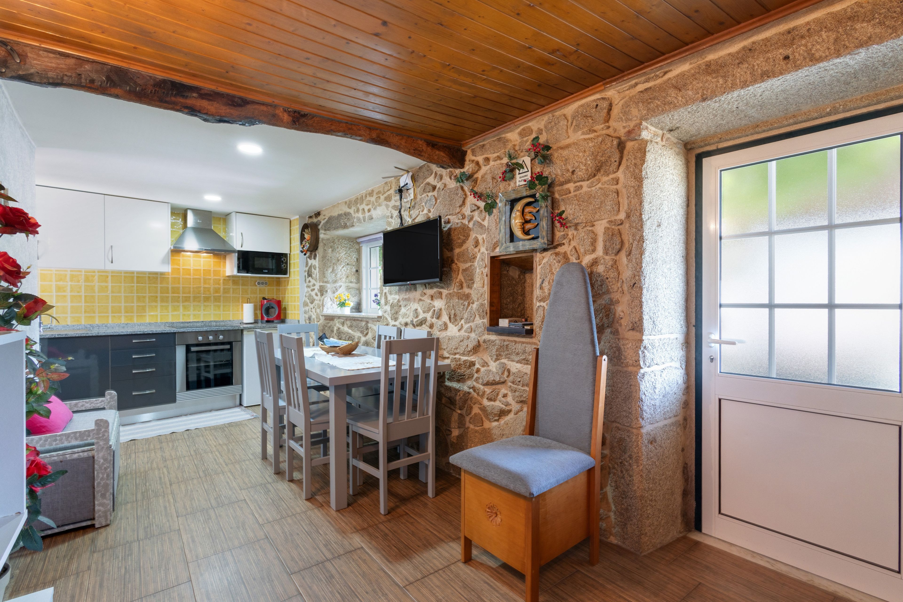 Una cocina con paredes de piedra, un comedor con mesa y sillas, y un televisor instalado en la pared.