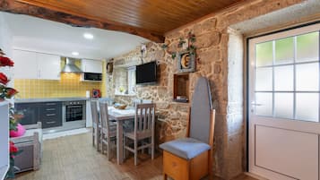 Una cocina con paredes de piedra, un comedor con mesa y sillas, y un televisor instalado en la pared.