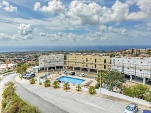 A hotel with a swimming pool, multiple floors, and a view of the surrounding town and coastline. - Peyia Pearl 21 – Sea View Studio (Pegeia)