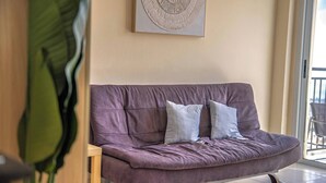 Un salon moderne avec un canapé violet, deux coussins, une table d’appoint en bois et une grande œuvre d’art abstraite accrochée au mur.