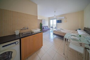 A hotel room with a kitchenette, a bed, a dining table set for two, and a balcony with a view.
