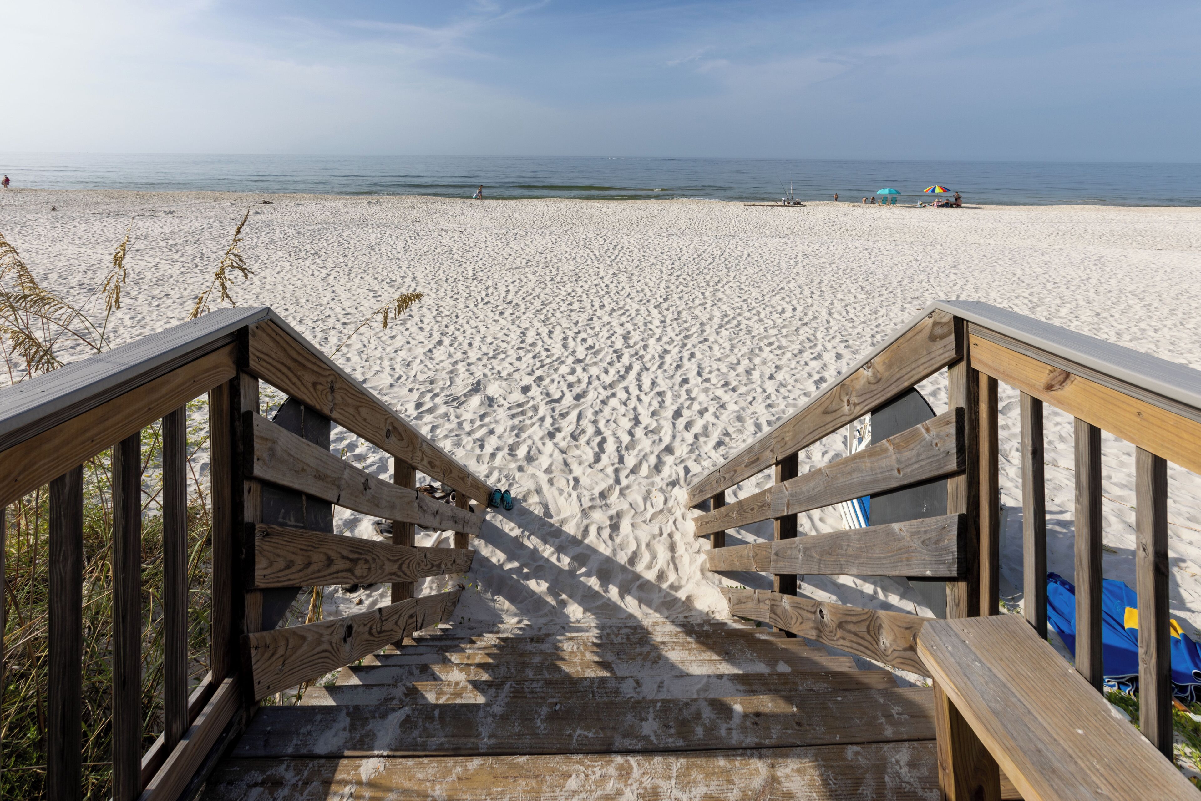 A wooden staircase leading to a sandy beach with a clear view of the ocean.