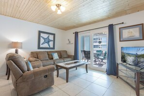 A living room with a sofa, armchair, and coffee table. There is a starfish artwork on the wall, a lamp, and a view of the outside balcony. - Lagoon Run 106 - Best of Both Worlds: Beach Access & Lagoon Dock! (Gulf Shores)