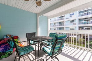 Ein Balkon mit weißer Reling, einem Tisch und zwei Stühlen mit gestreiften Kissen.