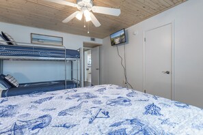 Ein Zimmer mit Etagenbetten, Deckenventilator, Fernseher und einer Tür.