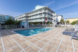 Ein Hotel mit Schwimmbad, mehreren Balkonen und einem umzäunten Bereich mit Liegestühlen.