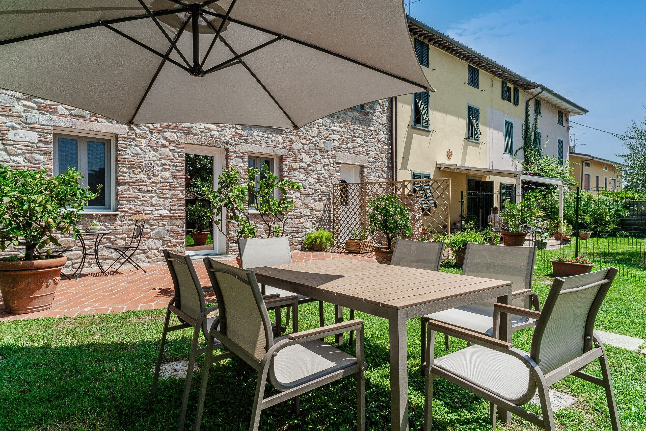An outdoor patio area with a table and chairs, surrounded by potted plants and a stone wall.