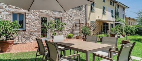 Un patio al aire libre con una mesa y sillas, rodeado de plantas en macetas y un muro de piedra.