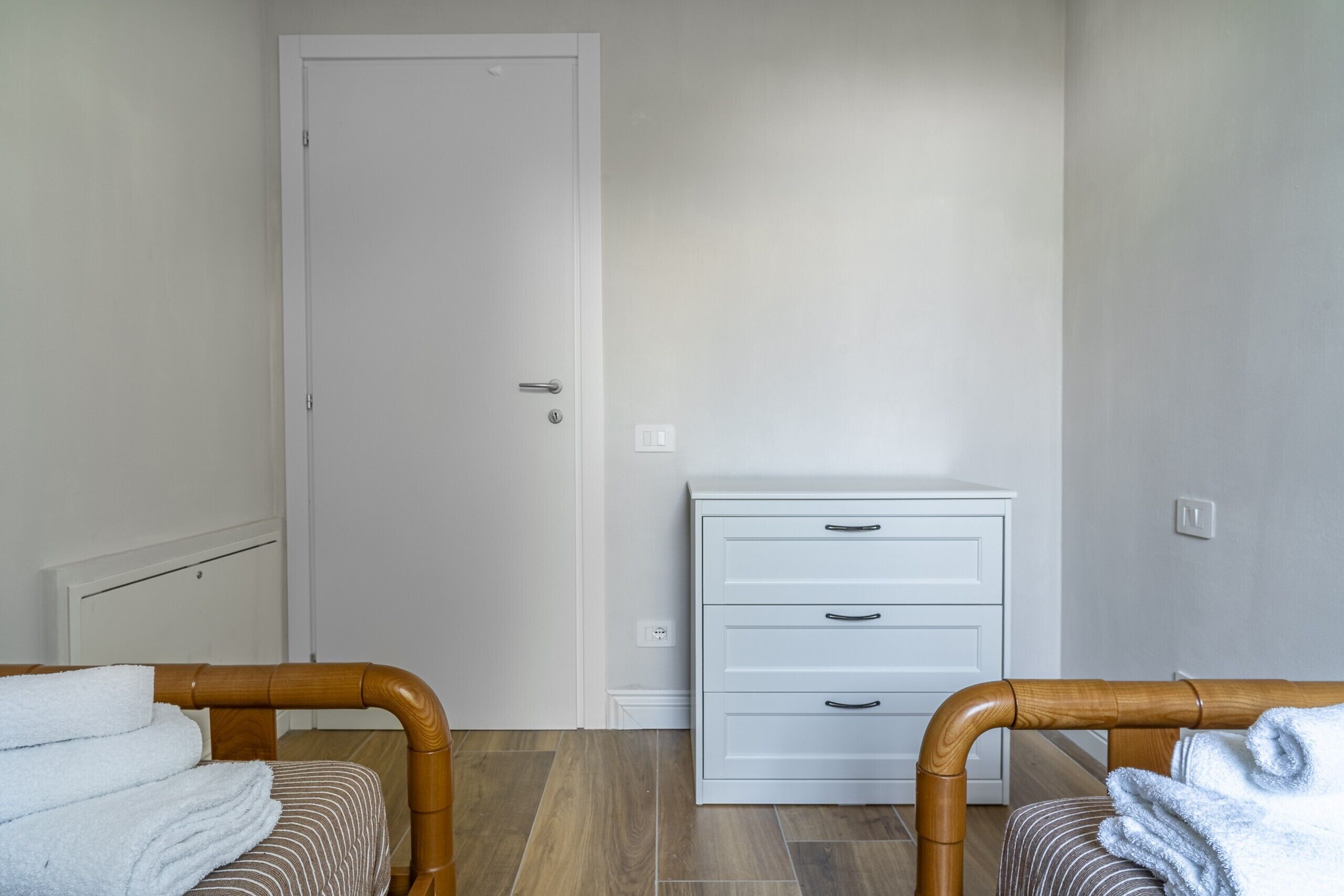 A room with two wooden chairs, a white bedside table, a white dresser, and a closed door.