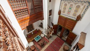 A traditional interior with a high ceiling, a wooden lattice partition, a patterned wall hanging, and a central chandelier. - Dar Rass Jnane (Fes)
