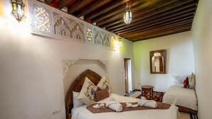 A hotel room with a wooden ceiling, a bed with white bedding, a small table, and a decorative wall. - Dar Rass Jnane (FES)