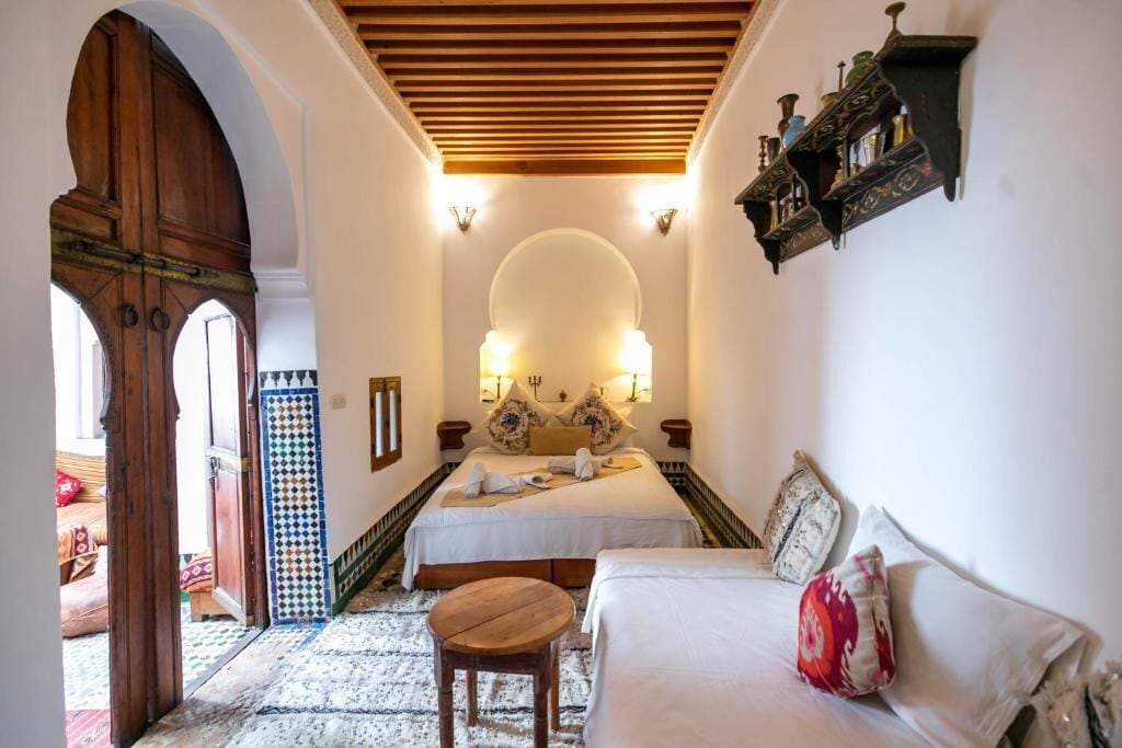 A hotel room with a bed, a sofa, a small wooden table, and a decorative mirror.