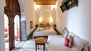 A hotel room with a bed, a sofa, a small wooden table, and a decorative mirror. - Dar Rass Jnane (FES)