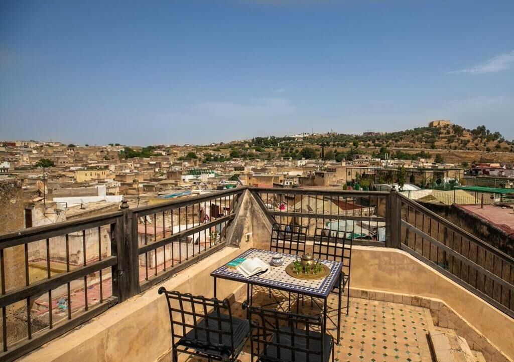 A terrace with a table and chairs, overlooking a cityscape with buildings and a hill.