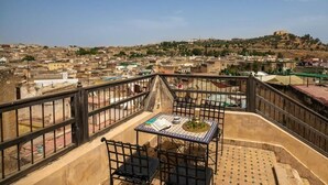 A terrace with a table and chairs, overlooking a cityscape with buildings and a hill. - Dar Rass Jnane (Fes)