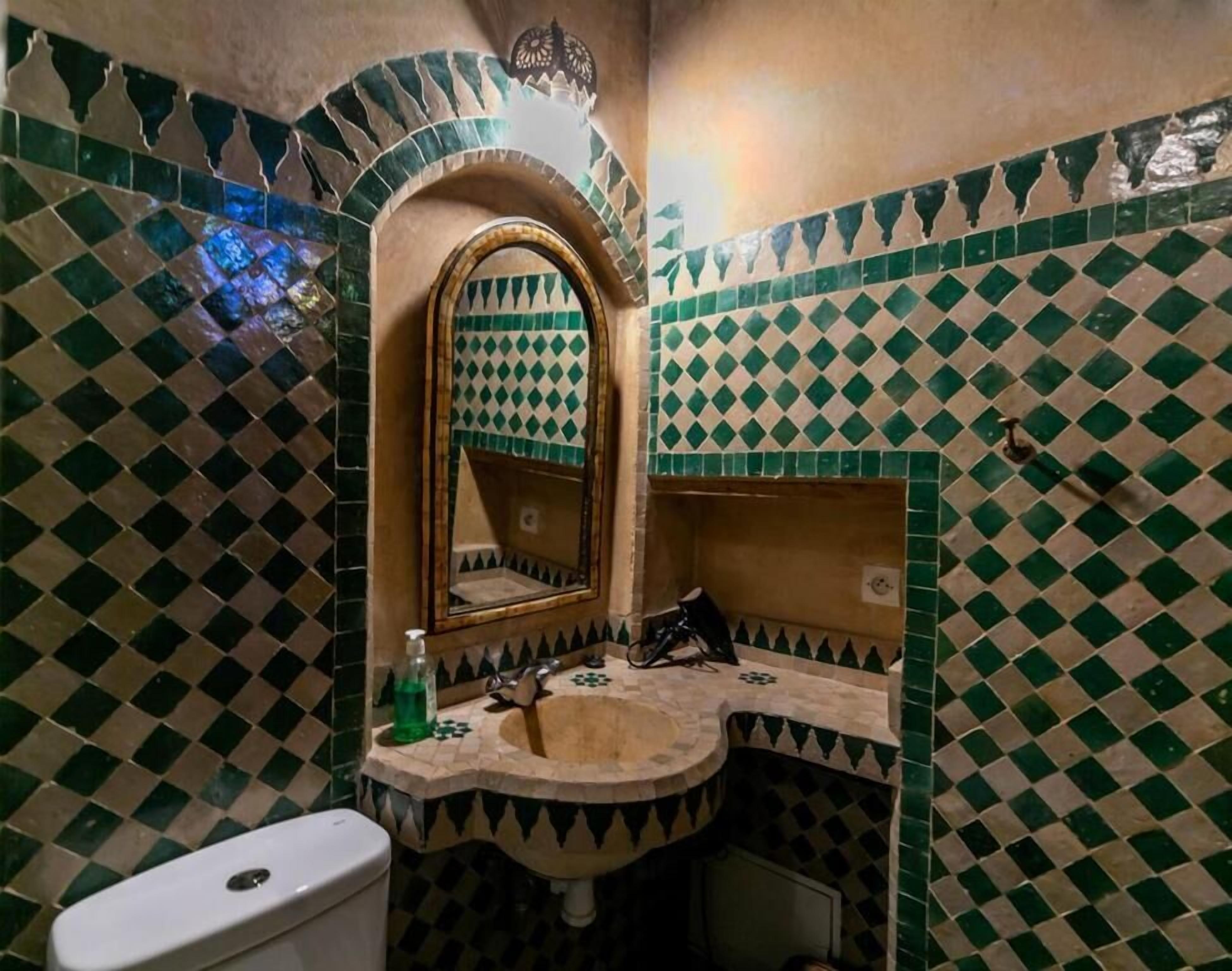 Um banheiro com piso de ladrilho xadrez, pia, espelho e vaso sanitário.