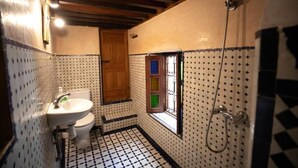 A bathroom with a tiled floor, a sink, a toilet, a shower, and a window with colored panes. - Dar Rass Jnane (FES)