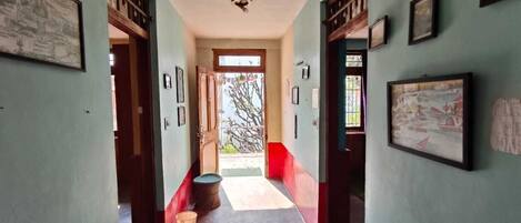 A hallway with framed pictures on the walls, a wooden door, and a window at the end.