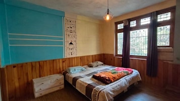 Um quarto com parede revestida de madeira, uma cama com colcha estampada, uma cômoda branca pequena e uma janela com cortinas.