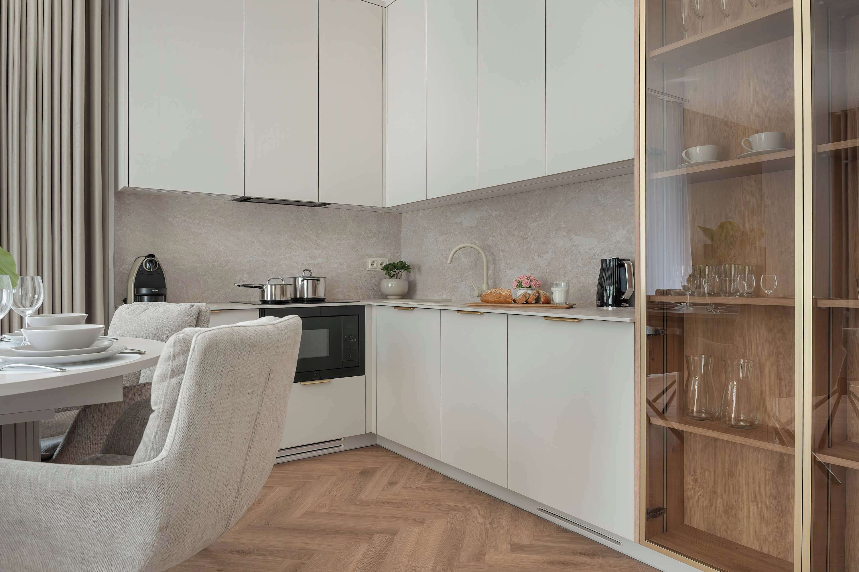 Una cocina moderna con armarios blancos, horno empotrado y comedor con mesa y sillas blancas.