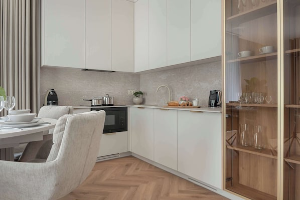 A modern kitchen with white cabinetry, a built-in oven, and a dining area with a white table and chairs.